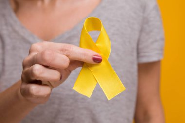 Endometriyozis, intihar önleme, sarkoma kemiği kanseri, mesane kanseri, karaciğer kanseri ve çocukluk kanseri konsepti için sarı altın kurdele farkındalığı sembolü taşıyan genç bir kadın. Sağlık hizmetleri. Kapat..