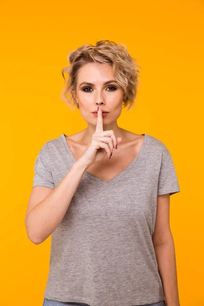Silence. Woman asking for silence or secrecy with finger on lips hush hand gesture yellow background wall. Pretty girl placing fingers on lips, shhh sign symbol. Negative emotion facial expression