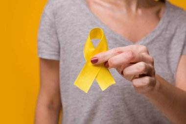 Endometriyozis, intihar önleme, sarkoma kemiği kanseri, mesane kanseri, karaciğer kanseri ve çocukluk kanseri konsepti için sarı altın kurdele farkındalığı sembolü taşıyan genç bir kadın. Sağlık hizmetleri. Kapat..