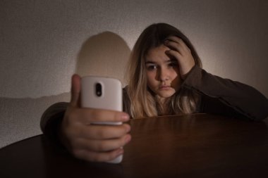 Bir cep telefonu bir karanlık ışık ile yatak odasında yatağın üstüne oturan ağıt tutmak tek üzücü teen