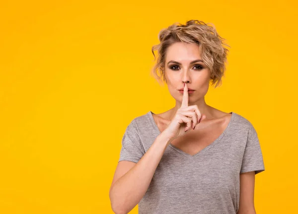 Silence. Woman asking for silence or secrecy with finger on lips hush hand gesture yellow background wall. Pretty girl placing fingers on lips, shhh sign symbol. Negative emotion facial expression