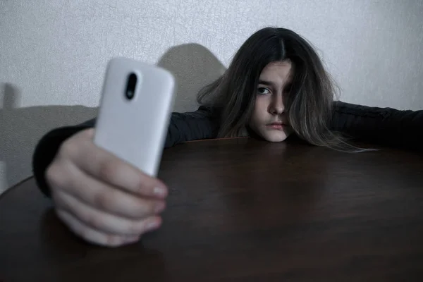 Egy szomorú tini gazdaság mobiltelefon siránkozik, ül az ágyon a hálószobában egy sötét fény — Stock Fotó