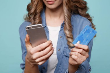 Cep telefonuyla kredi tutan mavi arka plan üzerinde izole heyecanlı genç bayan görüntüsünü