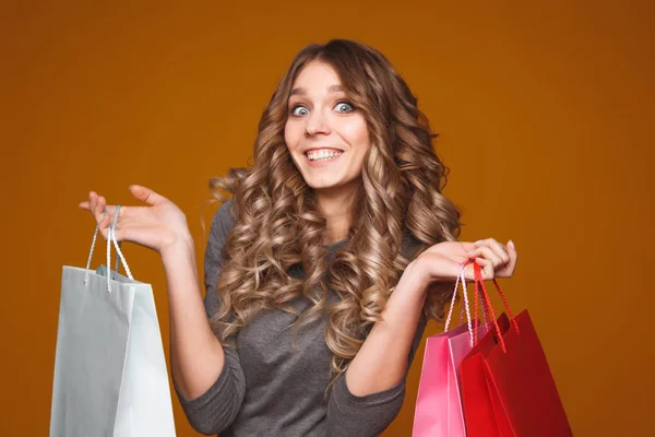 Foto van een vrolijke jonge brunette vrouw in witte zomer jurk bedrijf credit card poseren met boodschappentassen en camera kijken op roze achtergrond — Stockfoto