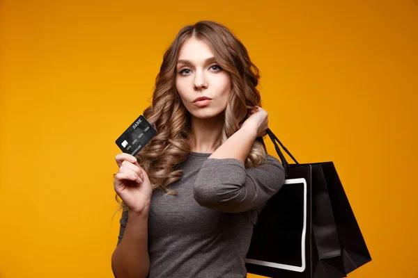 Ztratit up portrét šťastná mladá bruneta žena držící kreditku a barevné nákupní tašky, při pohledu na fotoaparát, izolované na žlutém podkladu — Stock fotografie