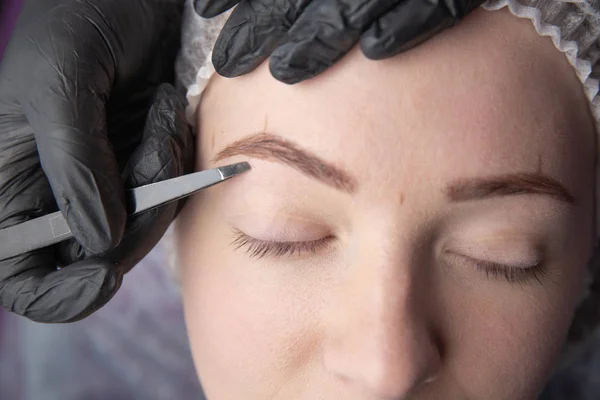 Young woman plucking eyebrows with tweezers close