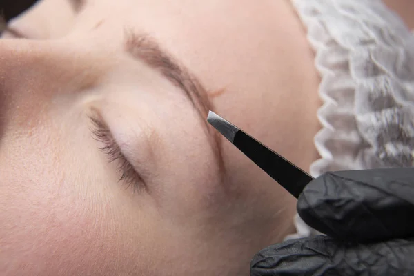 Young woman plucking eyebrows with tweezers close