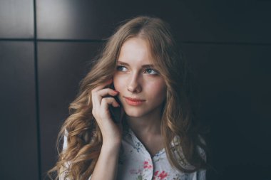 Genç ve güzel kadın konuşmak telefon karanlık duvarının yakınında bir bluz