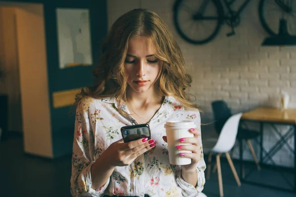 Immagine di giovane ragazza bionda carina con una tazza di caffè in possesso di telefono e testo di battitura, bella donna yong con unghie rosa brillante — Foto Stock