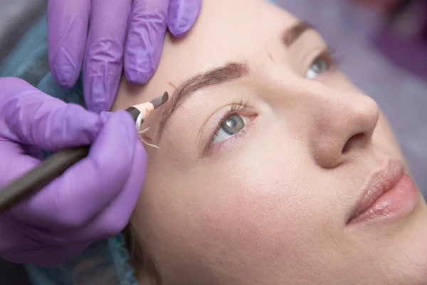 make-up for eyebrows of beautiful woman with thick brows in beauty salon. Closeup beautician doing tattooing eyebrow.