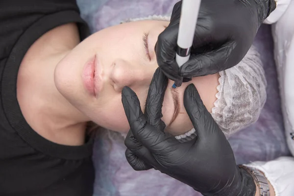 Maquiagem permanente para sobrancelhas. Testa de Microblading. Esteticista fazendo tatuagem de sobrancelha para rosto feminino. Menina bonita em uma beleza — Fotografia de Stock