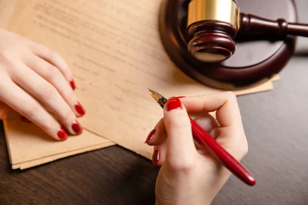 Advokat kvinna med ljusa röda maniqure sitter vid bord och skriva något av pen — Stockfoto