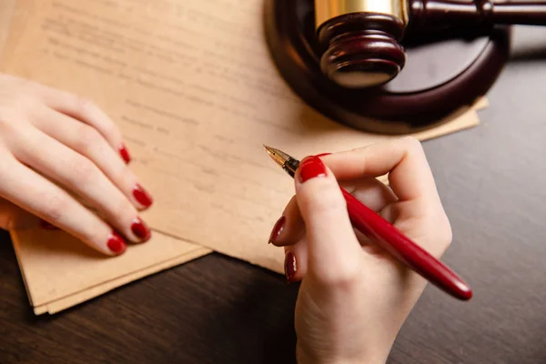 lawyer woman with bright red maniqure sitting at table and writing something by pen