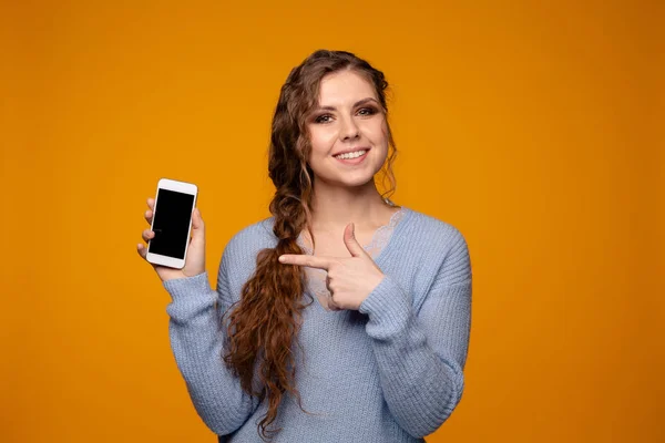 블루 스웨터 미소 하 고 그녀의 전화를 들고 있는 예쁜 여자 — 스톡 사진