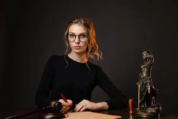 Young lawyer woman in a formal dress and spectacles sitting at table and writing something by pen, lawyer woman with bright red nails working isolated over the black backgrownd