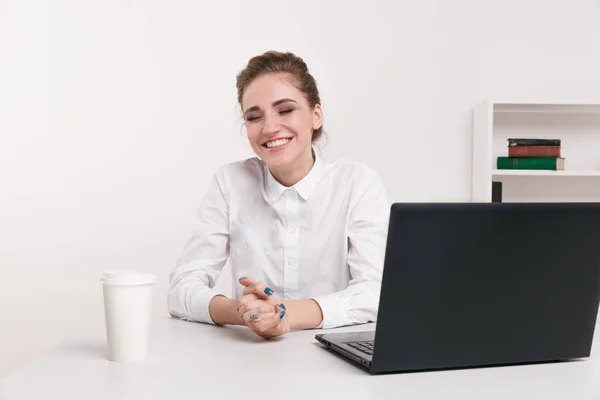 Una joven mujer de negocios con una blusa blanca sentada en una oficina. Trabajador de oficina sentado frente a una computadora negra. Café en la oficina . — Foto de Stock