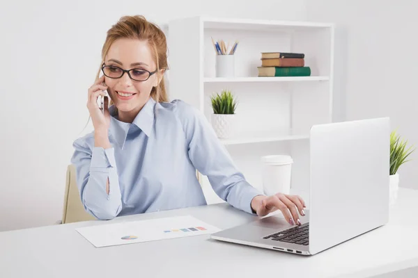 Mooie blonde kantoor meisje praten telefoon op haar werkplek. — Stockfoto