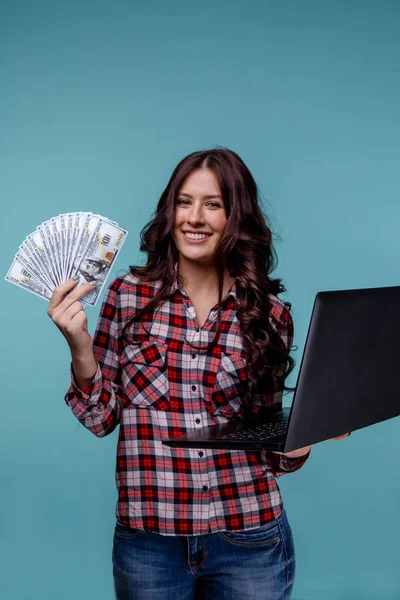 Bella donna holdina soldi e laptop guardando la fotocamera isolata sullo sfondo blu . — Foto Stock
