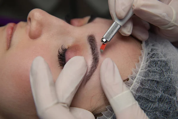 Maquiagem permanente para sobrancelhas. Testa de Microblading. Esteticista fazendo tatuagem de sobrancelha para rosto feminino. Menina bonita em uma beleza — Fotografia de Stock