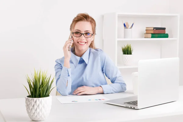 Mooie blonde kantoor meisje praten telefoon op haar werkplek. — Stockfoto