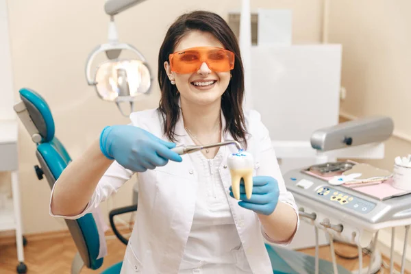 Dentista femminile nella maschera che mostra come fare la limatura dei denti sul modello di dente . — Foto Stock