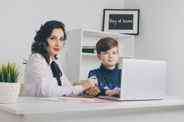 Öğretmen ve çocuk beyaz sınıfta ödevlerini yapıyor. Bir dizüstü bilgisayarda yazarak ev ödevi.