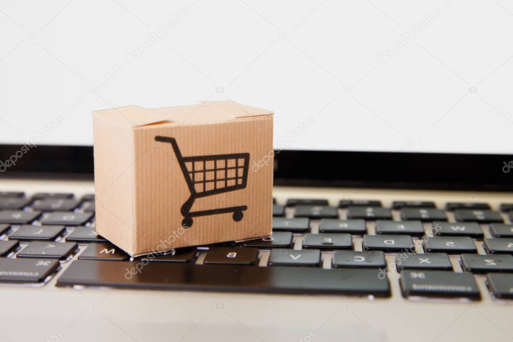 Online shopping . ecommerce and delivery service concept : Paper cartons with a cart or trolley logo on a laptop keyboard, depicts customers order things from retailer sites via the internet