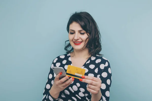 Jonge dame geïsoleerd op blauwe achtergrond met behulp van de mobiele telefoon bedrijf van de creditcard. — Stockfoto