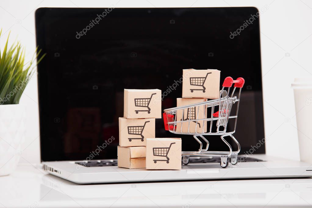 Online shopping ecommerce and delivery service concept : Paper cartons with a shopping cart or trolley logo on a laptop keyboard, depicts customers order things from retailer sites via the internet