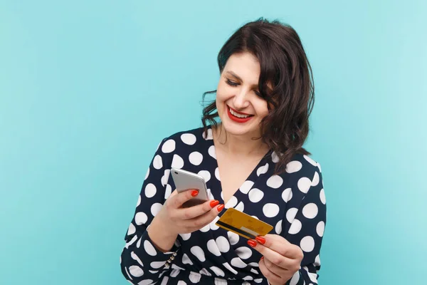 Jonge dame geïsoleerd op blauwe achtergrond met behulp van de mobiele telefoon bedrijf van de creditcard. — Stockfoto