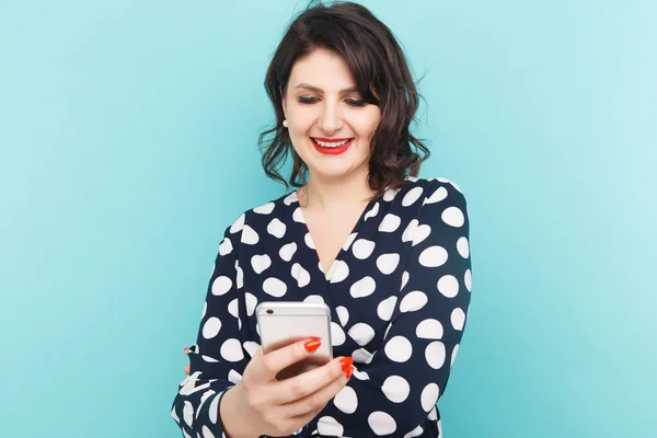 Woman holding phone and typing isolated over the blue background in the studio.