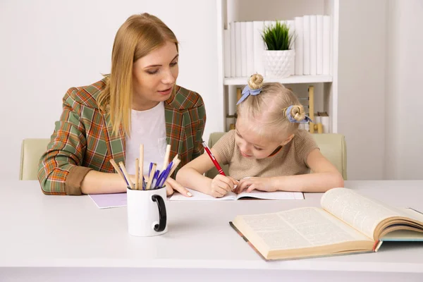Mutter unterrichtet kleine Tochter. Hausaufgaben zu Hause machen. — Stockfoto