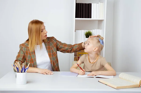 Sorrindo mãe com daugter sentados juntos na mesa e fazendo lição de casa . — Fotografia de Stock