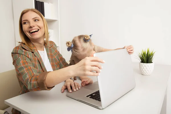 Χαρούμενη γυναίκα με παιδί που κάθεται στο γραφείο και χρησιμοποιεί φορητό υπολογιστή. — Φωτογραφία Αρχείου