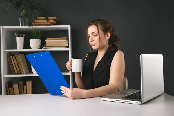 Female business worker in office drinking coffee and working sitting at the desk.