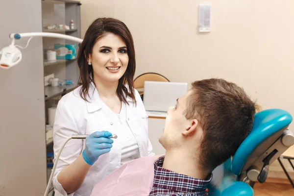 Immagine di una giovane dentista in camice bianco che lavora con un paziente di sesso maschile nella stanza dentale . — Foto Stock