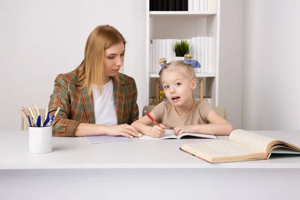 Mãe fazendo lição de casa com a filha em casa sentada na mesa . — Fotografia de Stock