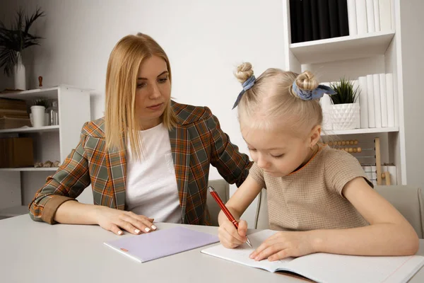 机の上で彼女の母親との就学前の女の子の書き込みタスク. — ストック写真