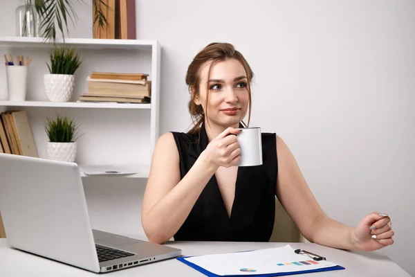 Woman in office drinking coffee at her workplace near the computer.