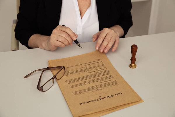 Женская рука с ручкой и нотариальной бумагой. Очки и печать на столе
.