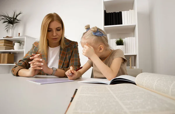 机の上で彼女の母親との就学前の女の子の書き込みタスク. — ストック写真