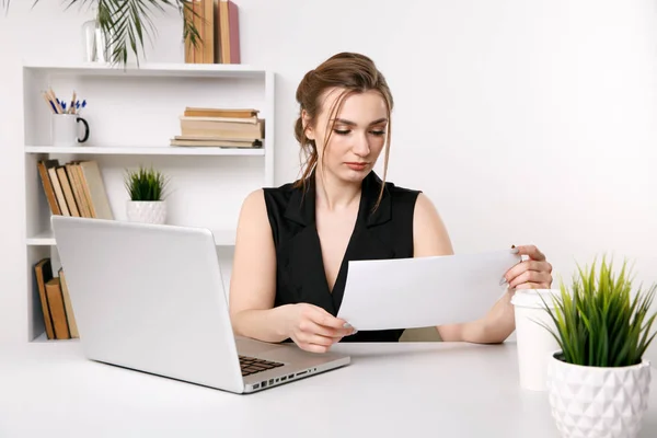 Mujer bastante joven trabajando con documentos sentados frente a su computadora . — Foto de Stock