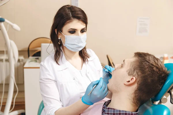 Imagen de una joven dentista en bata blanca trabajando con un paciente masculino en la sala dental . — Foto de Stock