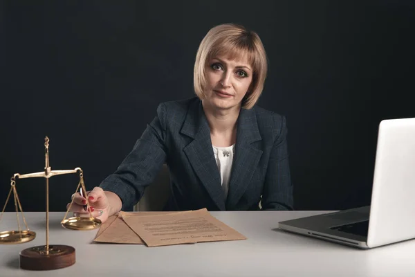 Rechtsanwältin arbeitet im Büro mit Dokumenten. Waage und Themis auf dem Schreibtisch. — Stockfoto