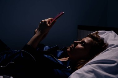 Kız yatakta yatan ve gece cep telefonu kullanarak.