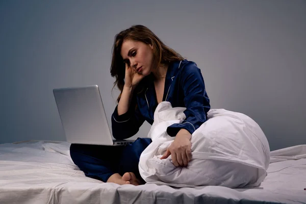 Imagen de hembra cansada y aburrida en casa sentada con computadora en la cama por la noche . —  Fotos de Stock