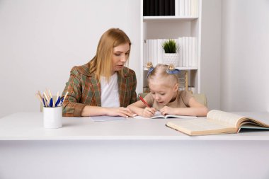 Anne ile evde çalışma masasında birlikte okuyan kız.