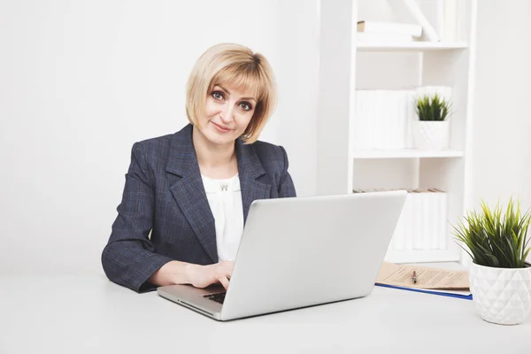 Aantrekkelijke blonde vrouw werkt op de laptop op haar werkplek. — Stockfoto