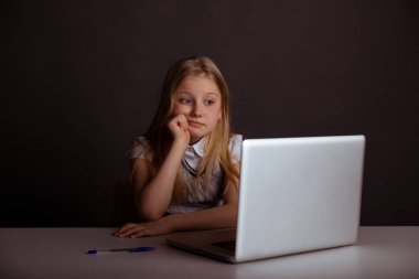 Sıkılmış küçük kız masada oturan ve bilgisayar izole kullanarak.