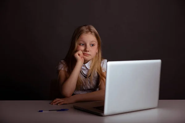 Vervelen klein meisje zittend op de tafel en het gebruik van computer geïsoleerd. — Stockfoto